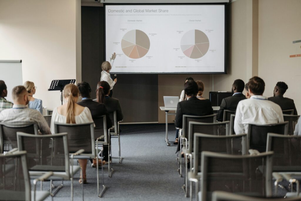 pexels-photo-8761520-8761520 Business conference with diverse audience and speaker presenting market data.